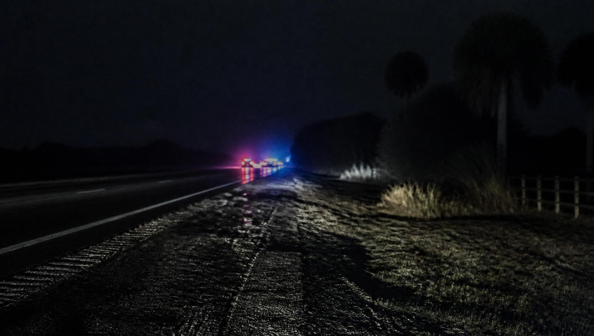 A dark Florida highway at night with distant emergency lights